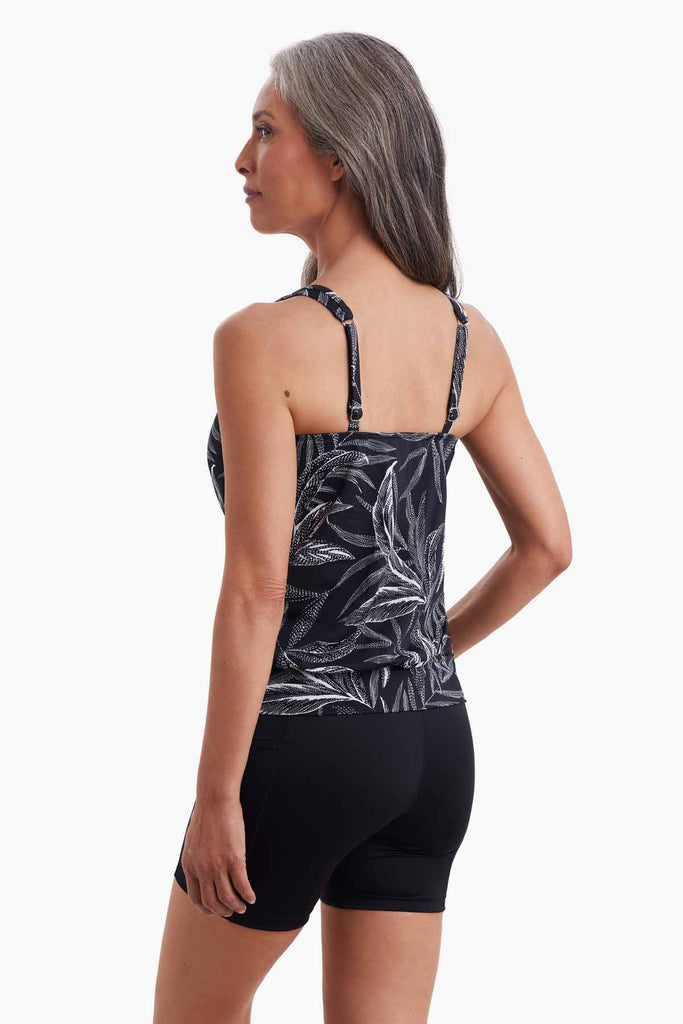 Woman turned left wearing a tankini top with a black and white palm leaf print