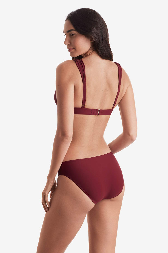 Woman turned left wearing a dark red bikini top and dark red swim bottoms