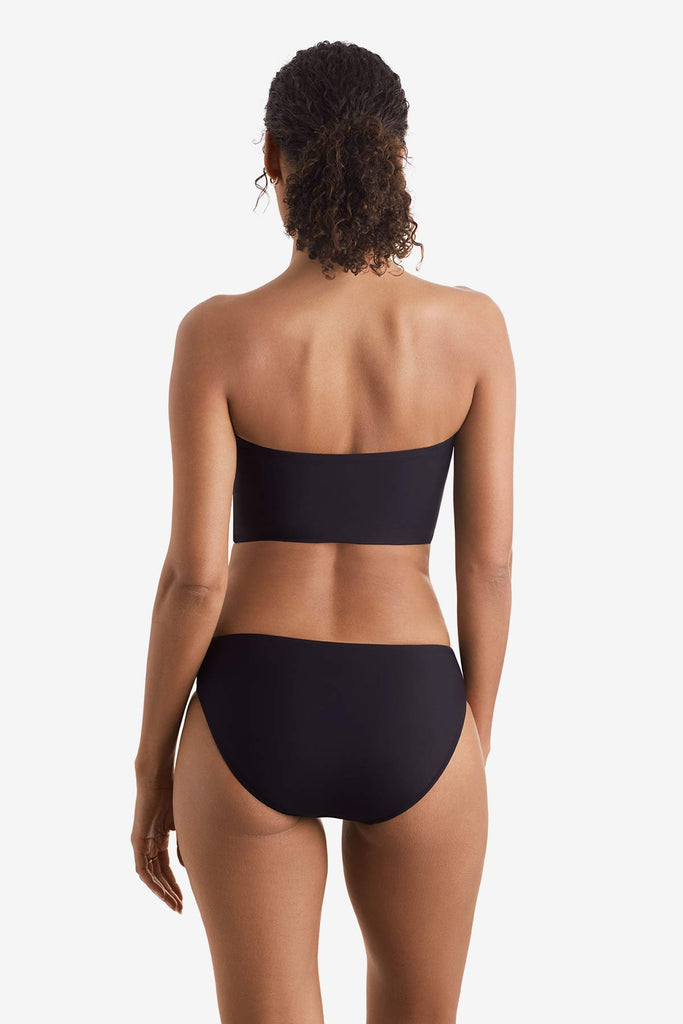 Woman faced away wearing a black midkini swim top with black swim bottoms