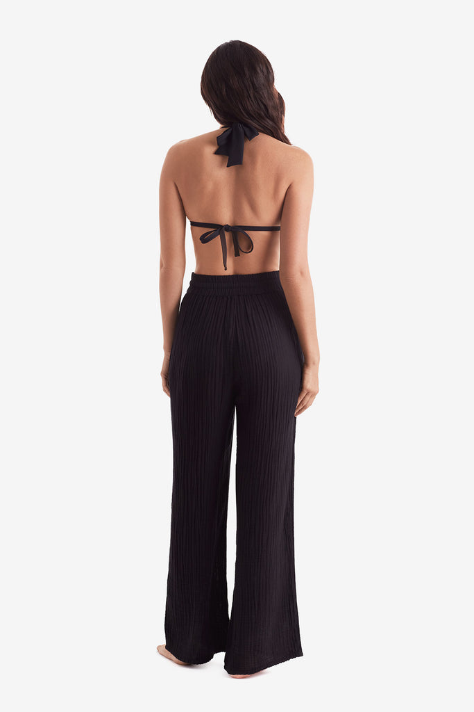 Woman faced away wearing a black bikini top and black beach pants
