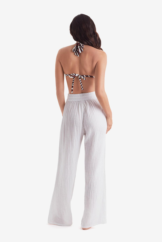 Woman turned away wearing a zebra print bikini top with white beach pants