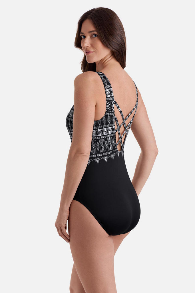 Woman turned left wearing a black and white tribal printed one-piece swimsuit with a cross back