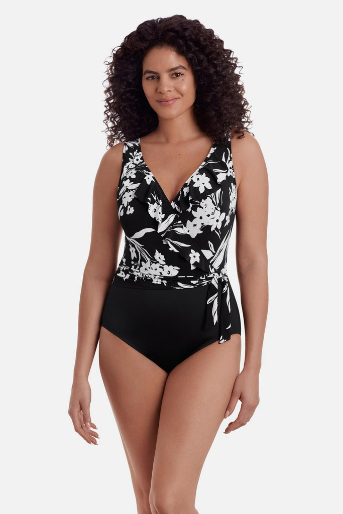 Woman wearing a black and white floral one-piece swimsuit with a side sash